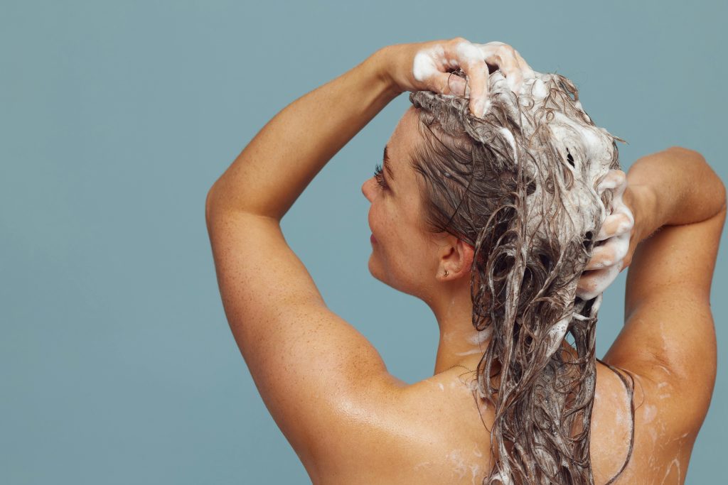 femme se lave les cheveux de dos avec du shampoing