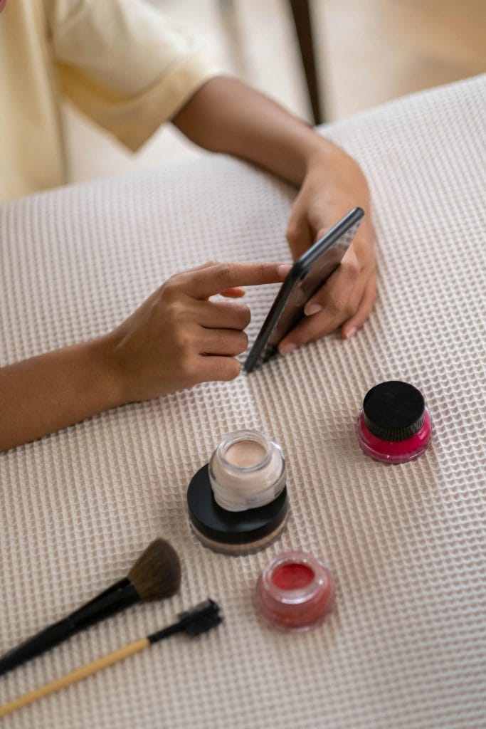 personne tenant un téléphone à côté de produits de maquillage