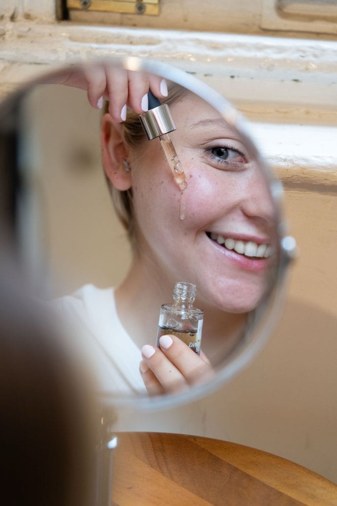 femme qui met du sérum sur son visage devant son miroir